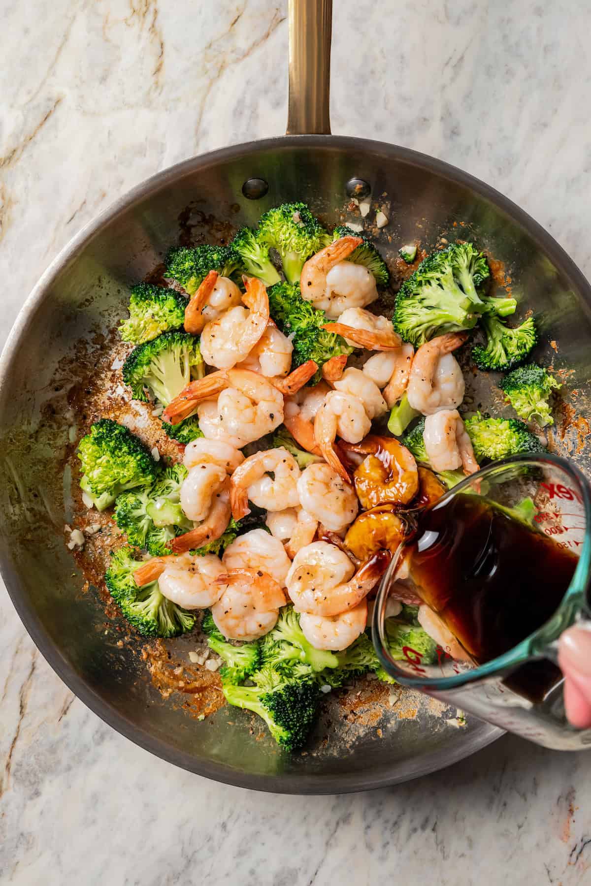 Stir fry sauce being poured over shrimp and broccoli in a skillet.