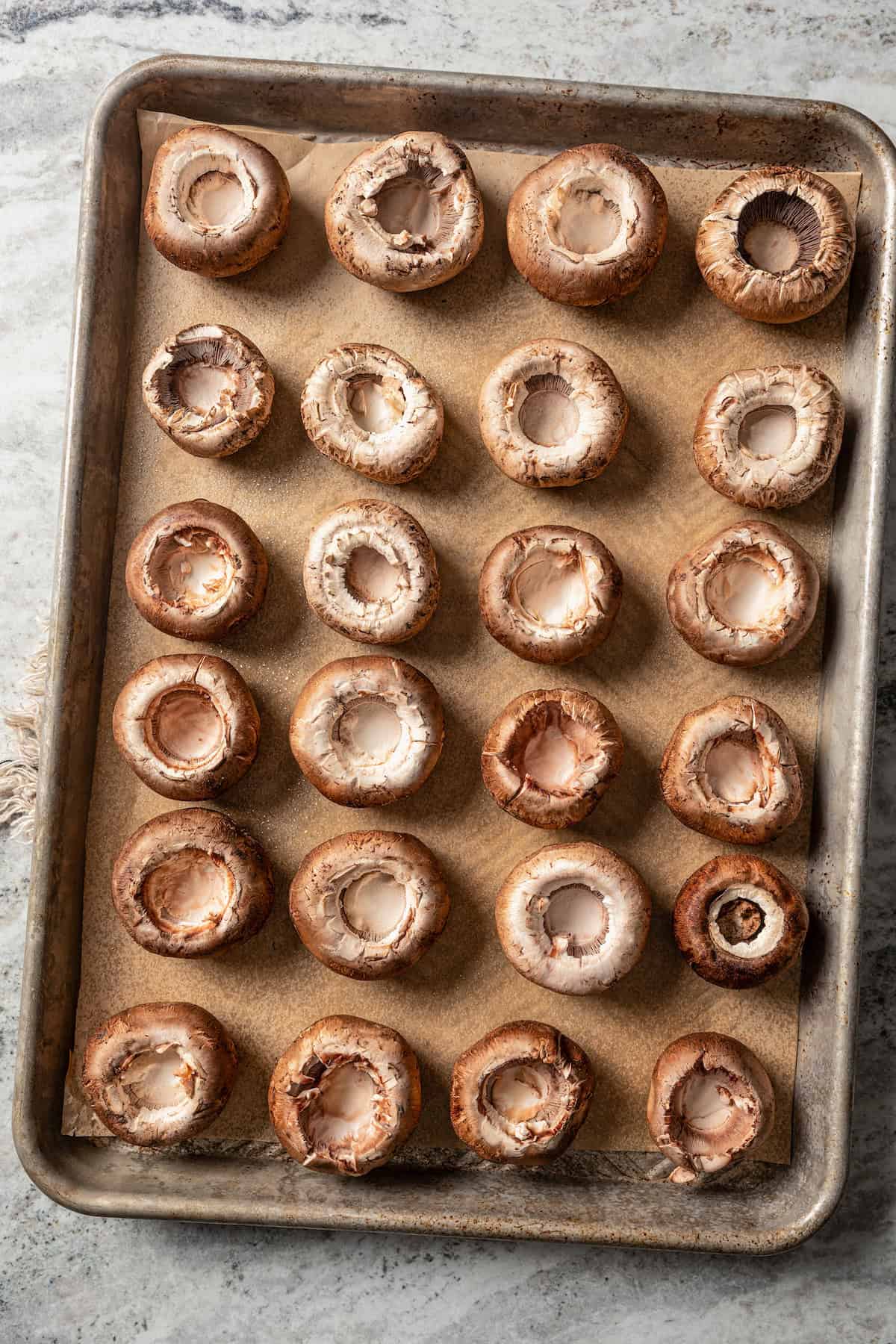 Rows of hollowed out mushroom caps on a lined baking sheet.