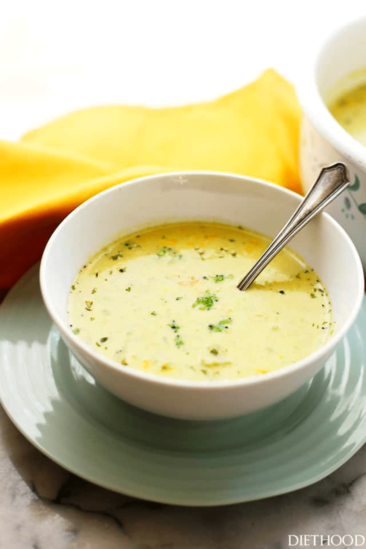 a white bowl filled with broccoli cheese soup and set on a blue plate.