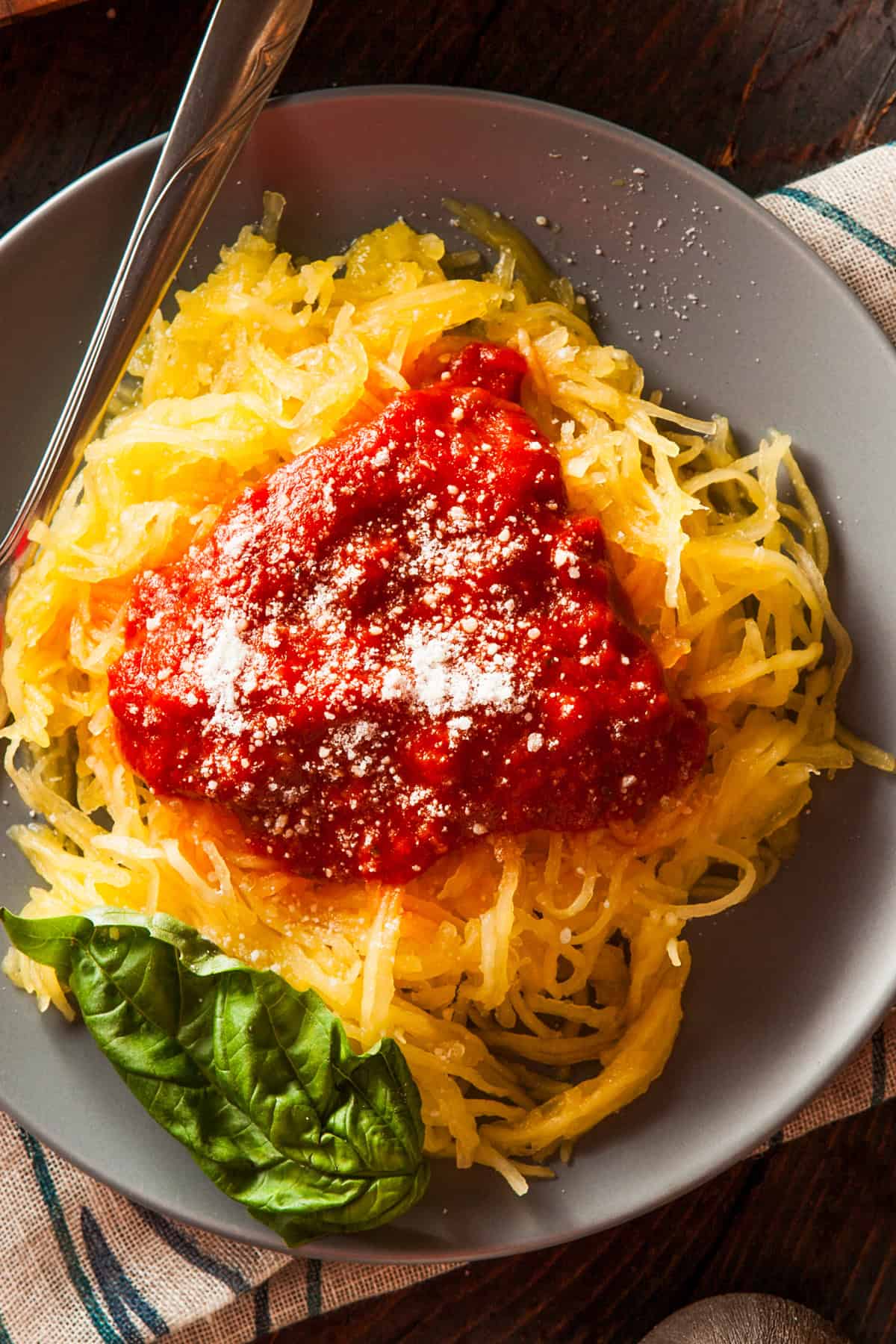 Cooked spaghetti squash served on a dinner plate and topped with Marinara Sauce and grated parmesan cheese.