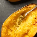 Baking sheet with cooked spaghetti squash and a fork shredding the squash.