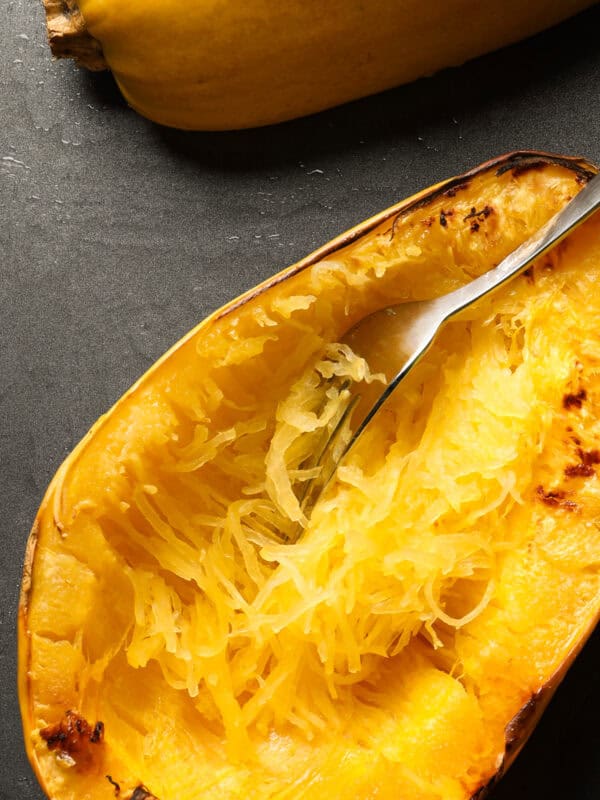 Baking sheet with cooked spaghetti squash and a fork shredding the squash.