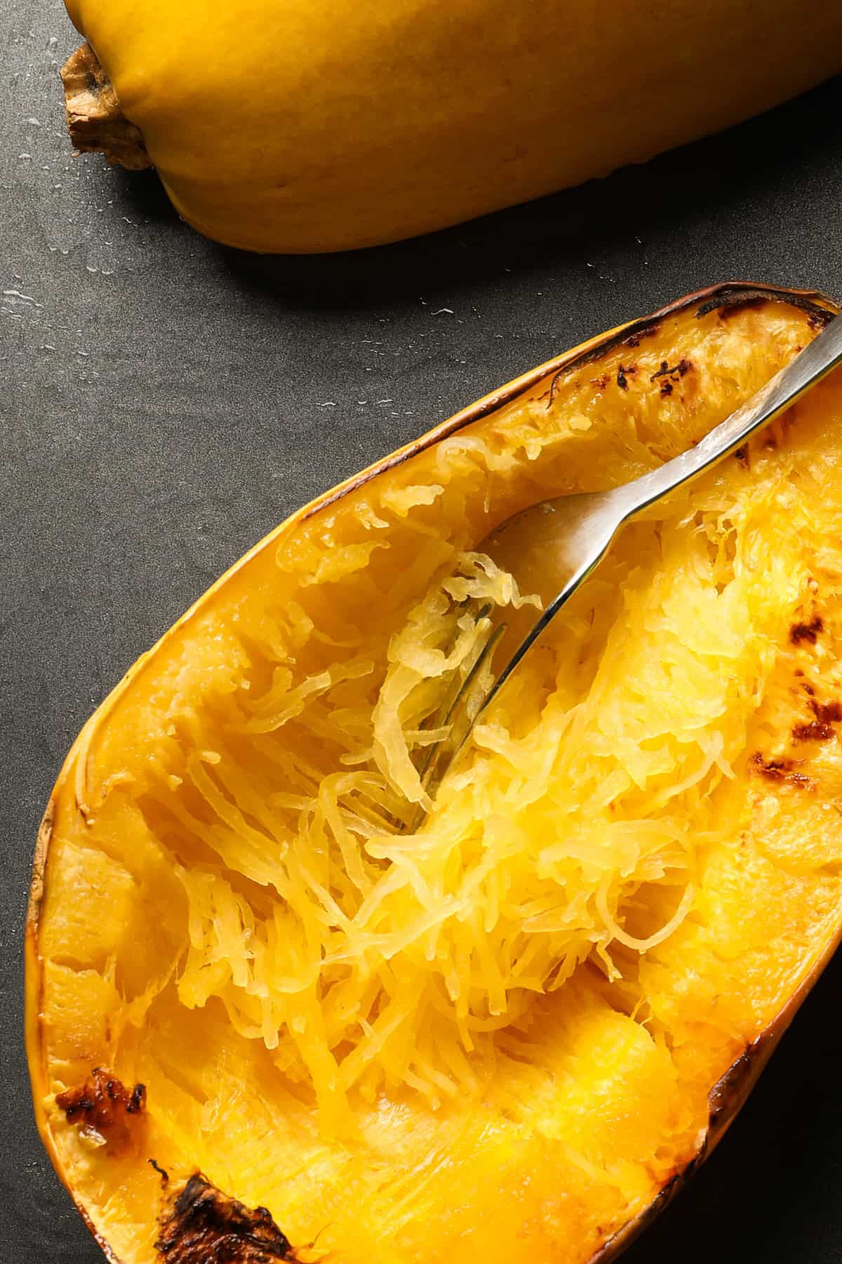 Baking sheet with cooked spaghetti squash and a fork shredding the squash.