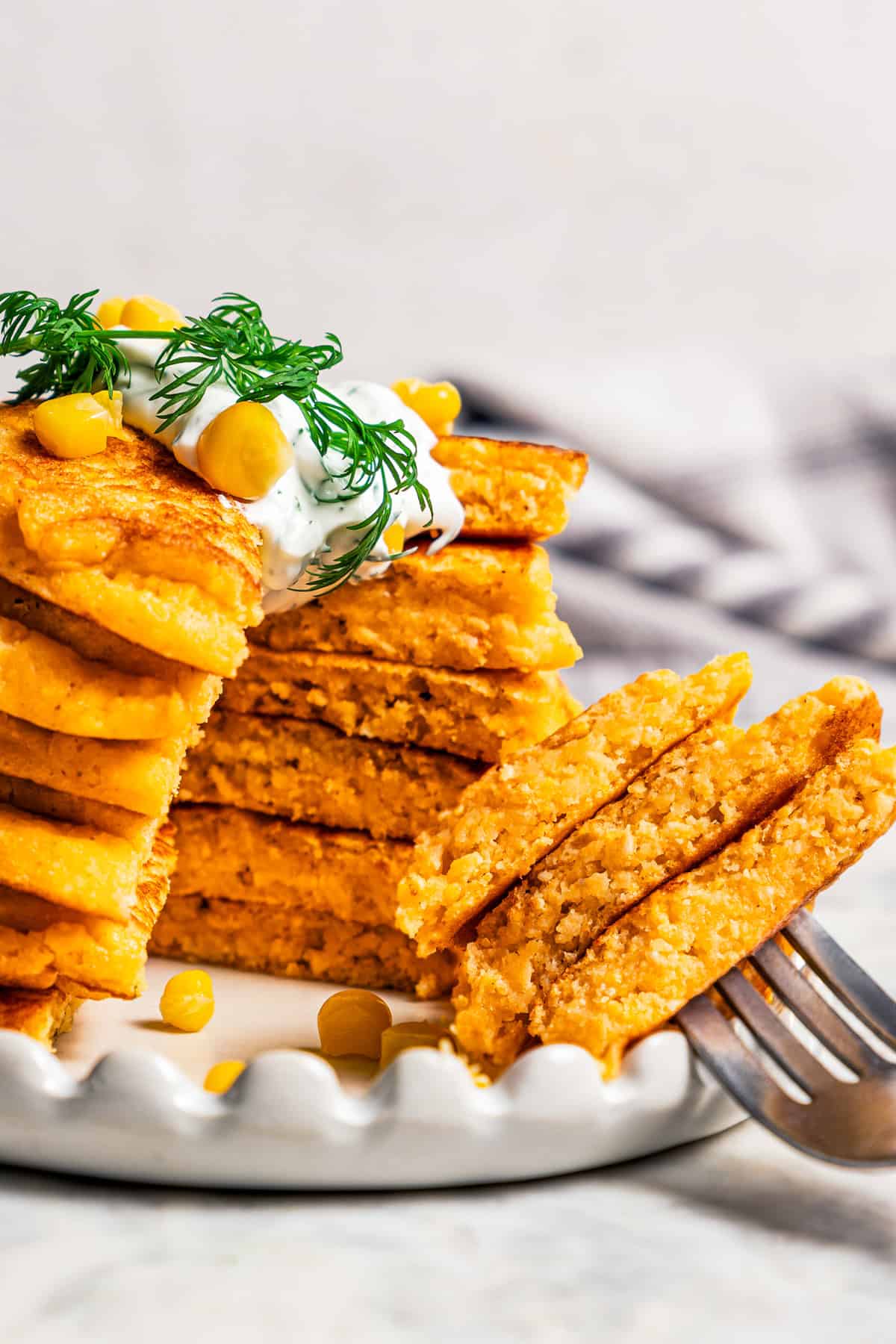 A stack of cornbread pancakes next to a forkful resting on a plate.