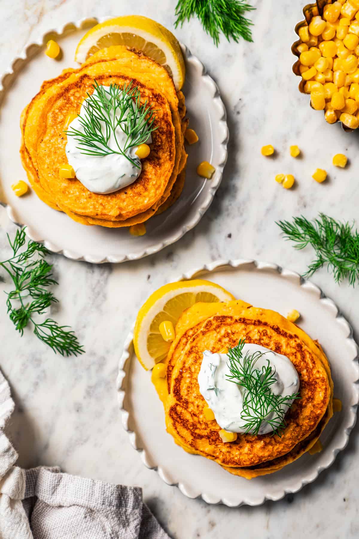 Overhead image of two plates with cornbread pancakes garnished with lemon dill sauce.