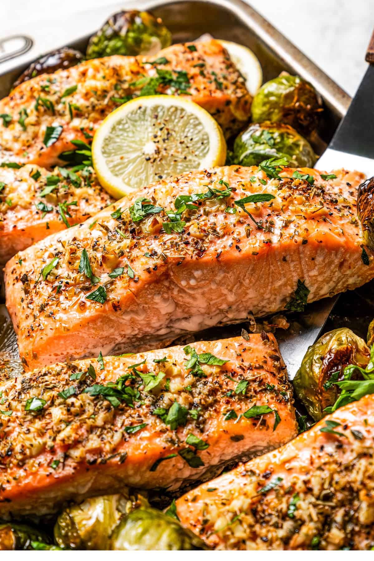 A spatula lifting a baked salmon fillet from a sheet pan.