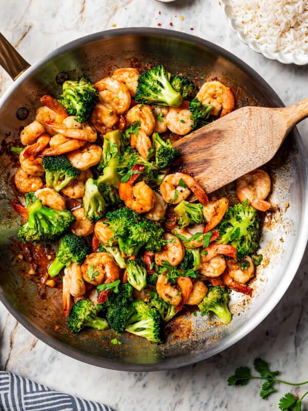 Wooden spoon stirring through shrimp stir fry in a skillet with broccoli.