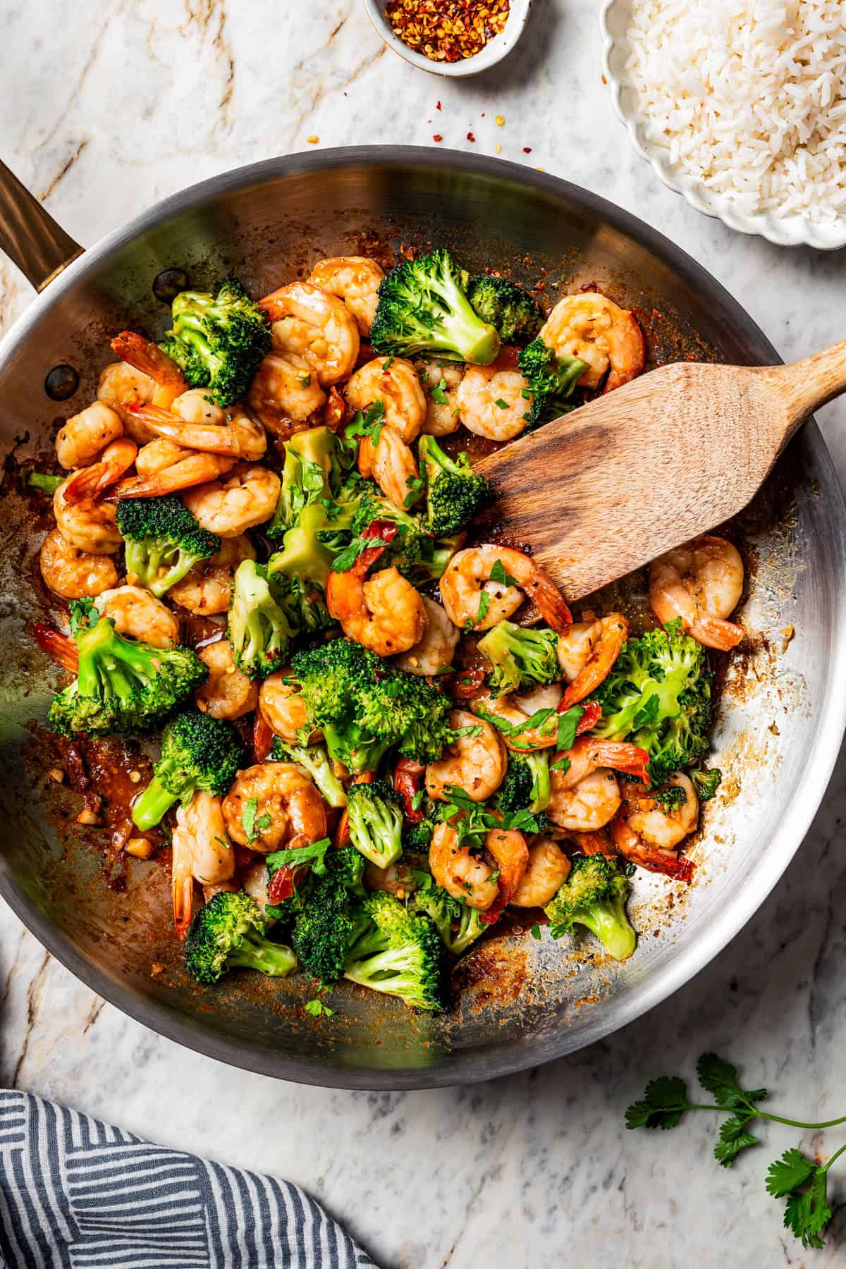 Wooden spoon stirring through shrimp stir fry in a skillet with broccoli.