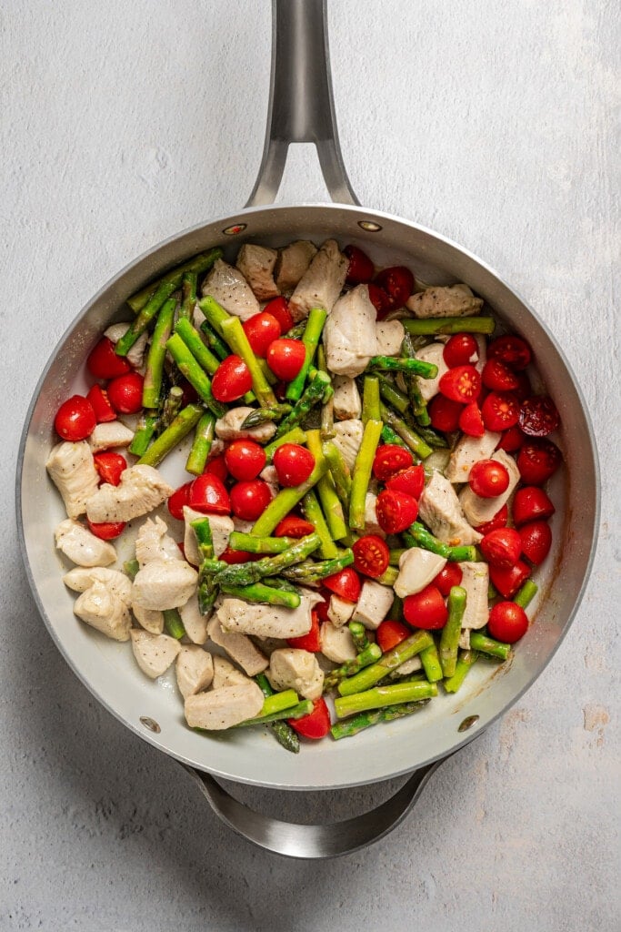 Sauteed chicken, asparagus, and cherry tomatoes on a skillet.
