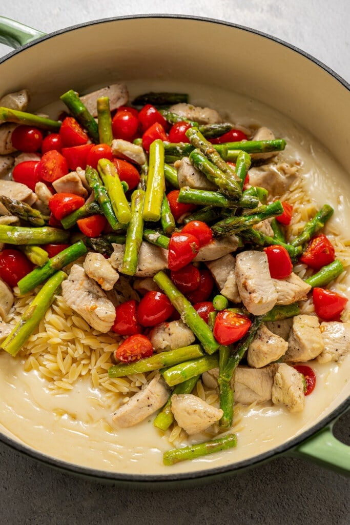 Cooked chicken, asparagus, and cherry tomatoes added to a large pot with orzo and cream sauce.