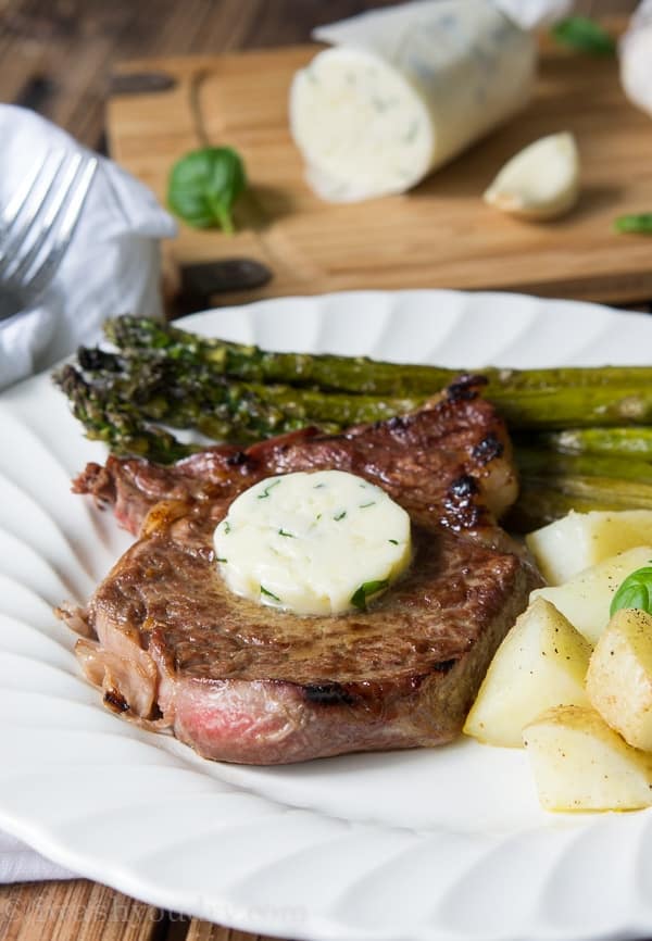 Steak topped with herbed butter on a plate with asparagus and potatoes