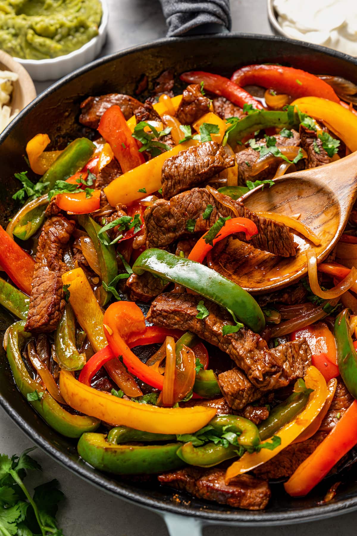Close up of steak fajitas in a cast iron skillet with a wooden spoon.
