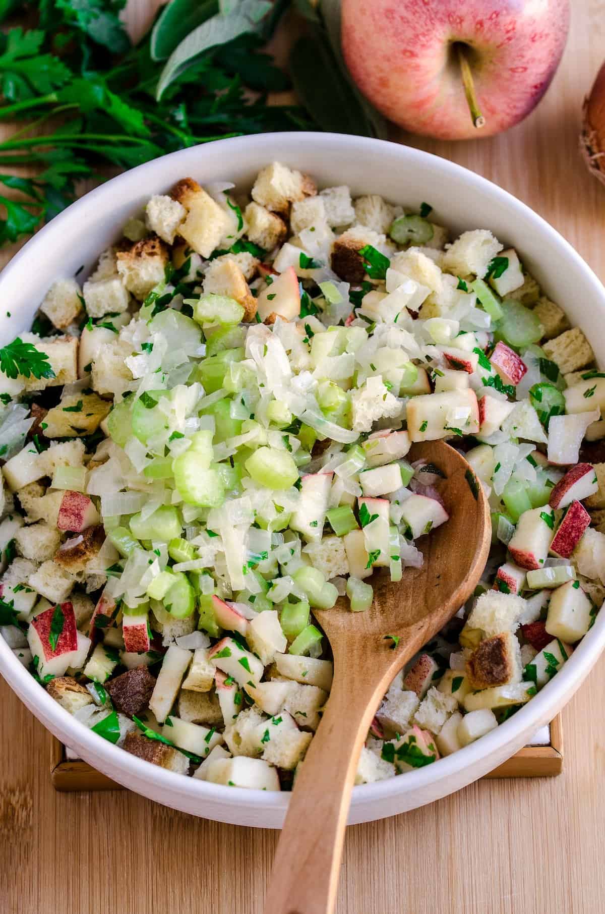 Mixing ingredients for apple stuffing in a white bowl with a wooden spoon