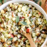 Apple stuffing in a white bowl with a wooden spoon topped with fresh sage