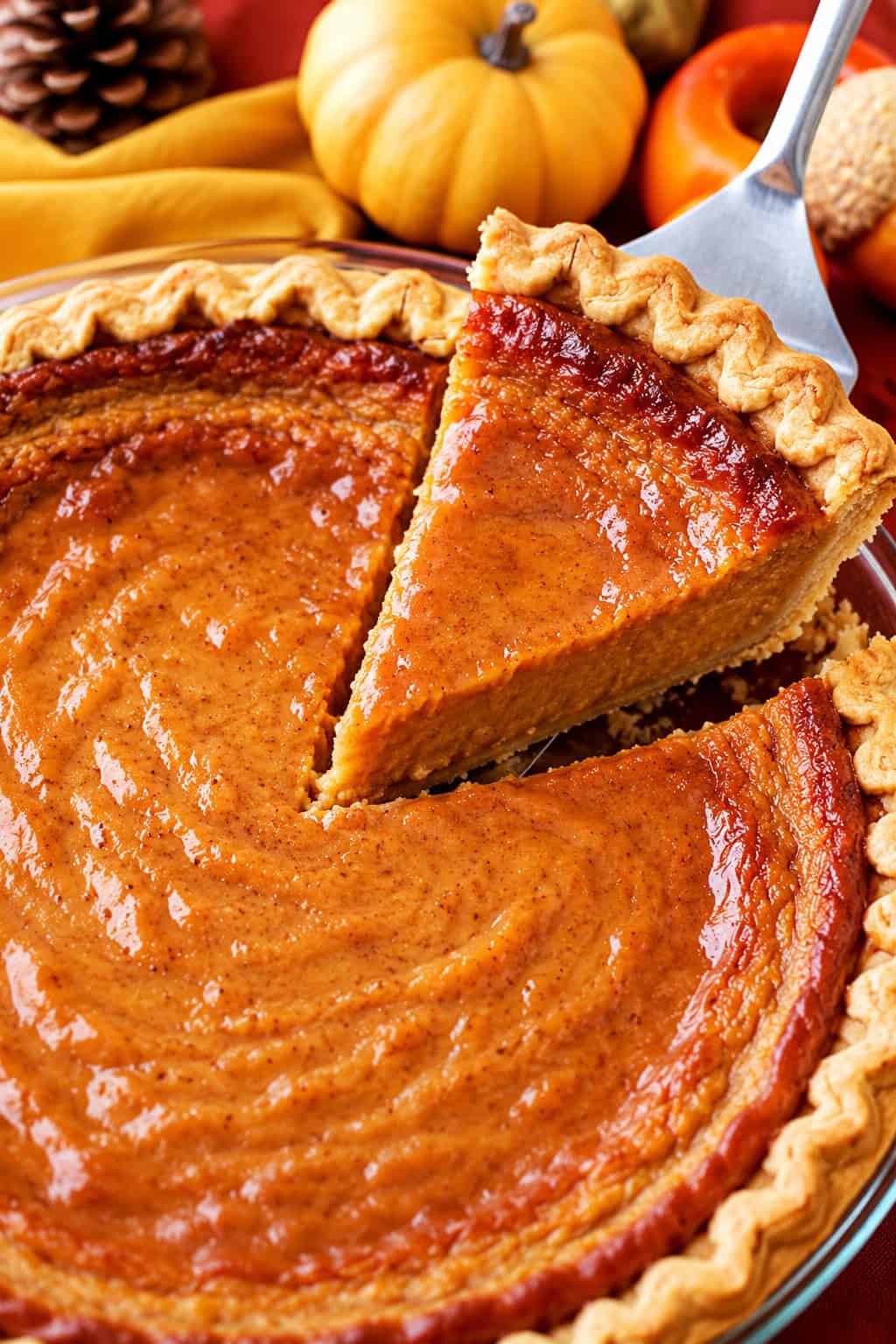 This easy pumpkin pie recipe is perfect for Thanksgiving dessert! It’s a rich and creamy pie with a lighter take on the classic treat. Lifting a slice of pumpkin pie with a server.