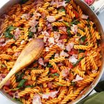 Wooden spoon stirring through cooked pasta in a skillet.