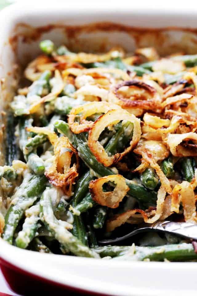 A spoonful of creamy green bean casserole is lifted from a baking dish.