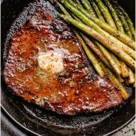 cooked steak with pat of butter on top and asparagus to the side