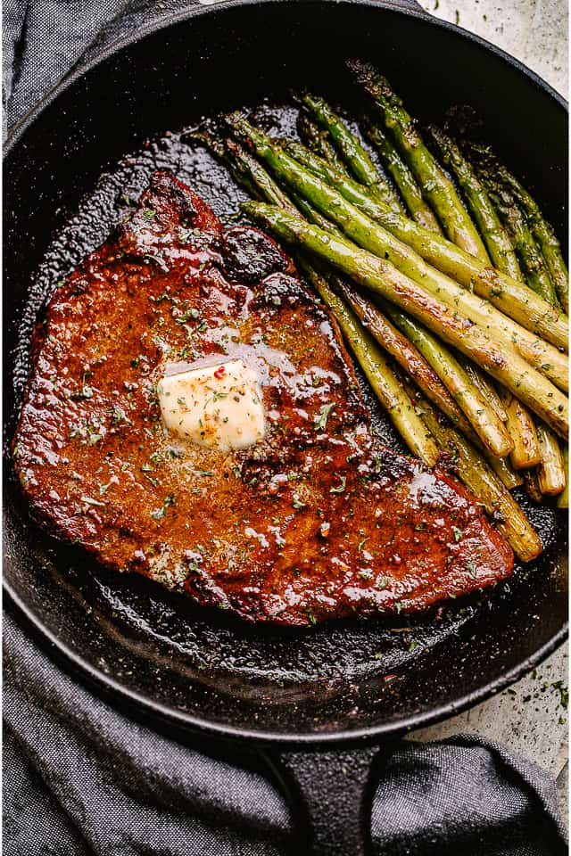 cooked steak with pat of butter on top and asparagus to the side