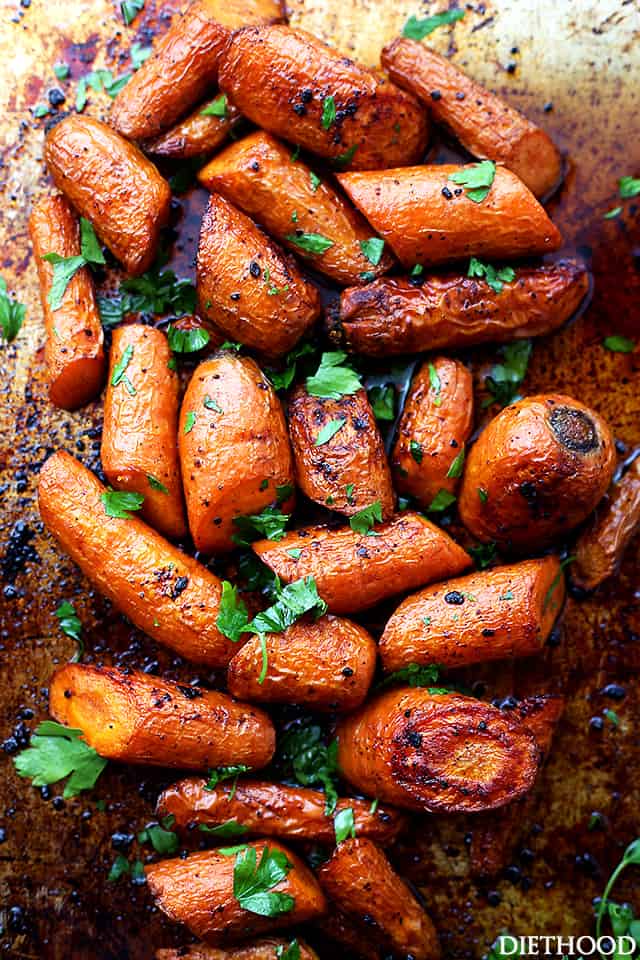 Roasting chopped carrots on a dark baking sheet.