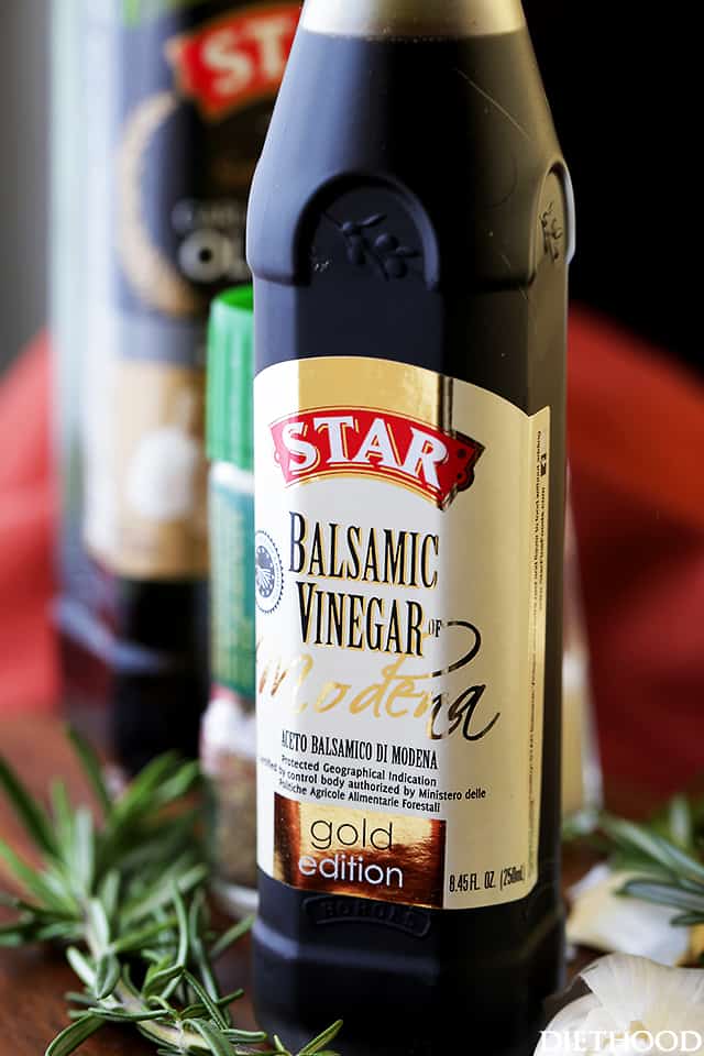 A bottle of balsamic vinegar next to a sprig of rosemary