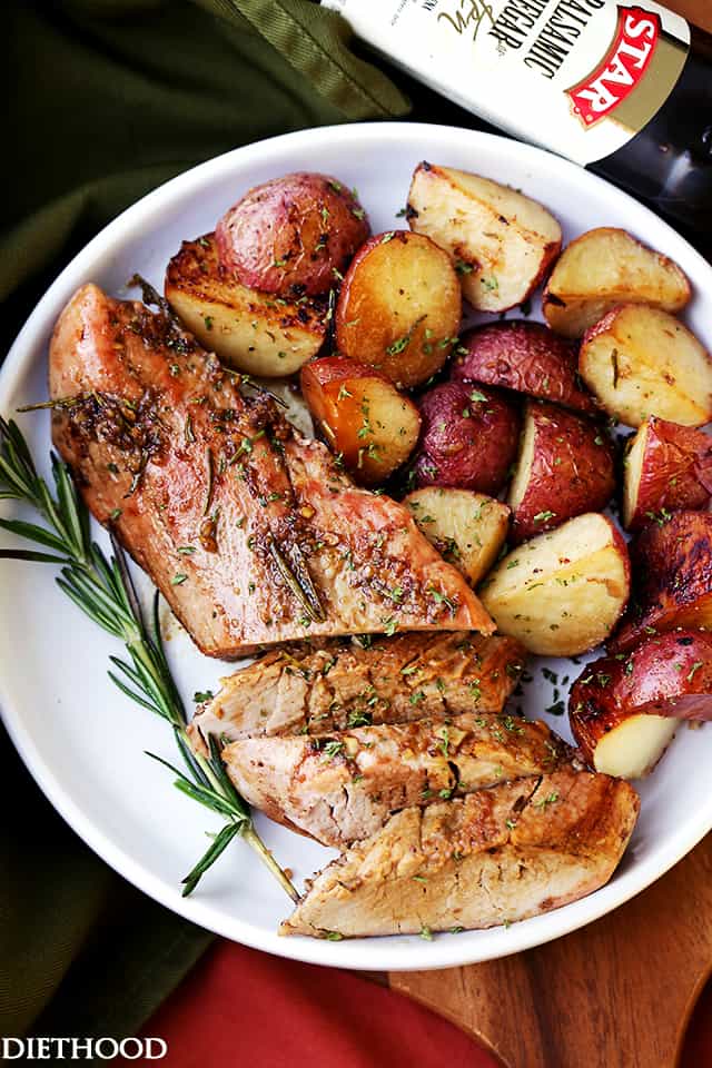 Partially sliced balsamic roasted pork tenderloin on a serving plate next to roasted potatoes and a sprig of rosemary