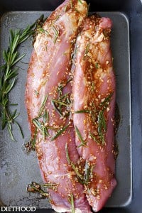 Two raw cuts of pork tenderloin in a roasting pan covered in garlic and rosemary balsamic glaze