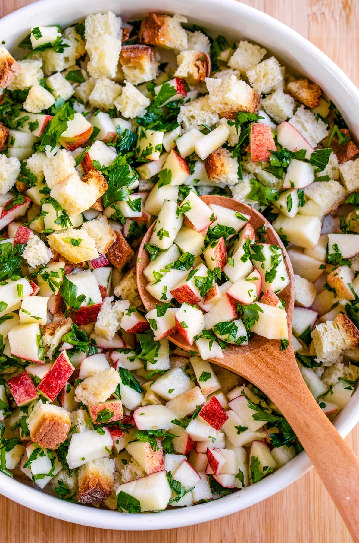 Mixing through diced apples, dried bread cubes, and fresh herbs in a bowl.
