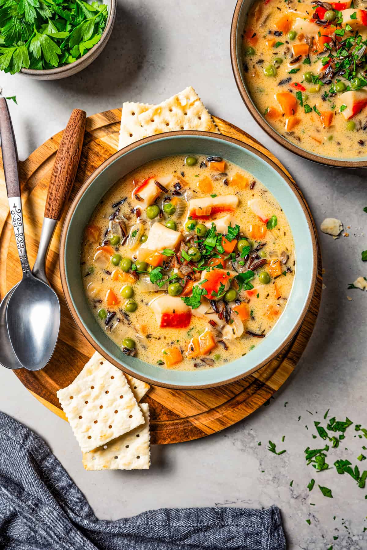 Overhead view of a bowl of crab soup next to saltine crackers and spoons, with a second bowl placed nearby.