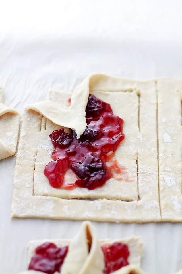 Shaping puff pastry dough into a bow, folding it over raspberry jam.