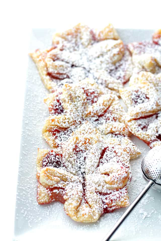 Raspberry Jam Puff Pastries arranged on a plate and dusted with powdered sugar.