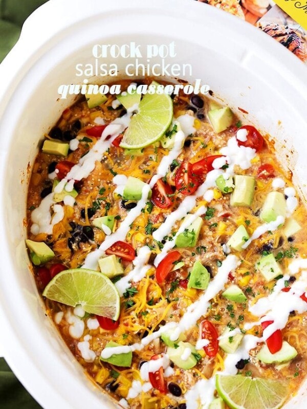 Overhead view of chicken quinoa casserole in a white crock pot drizzled with sour cream and garnished with lime wedges.