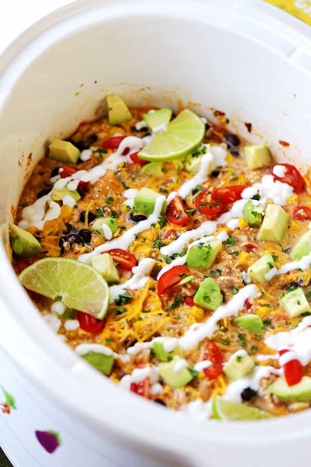 Overhead view of chicken quinoa casserole in a white crock pot drizzled with sour cream and garnished with lime wedges.