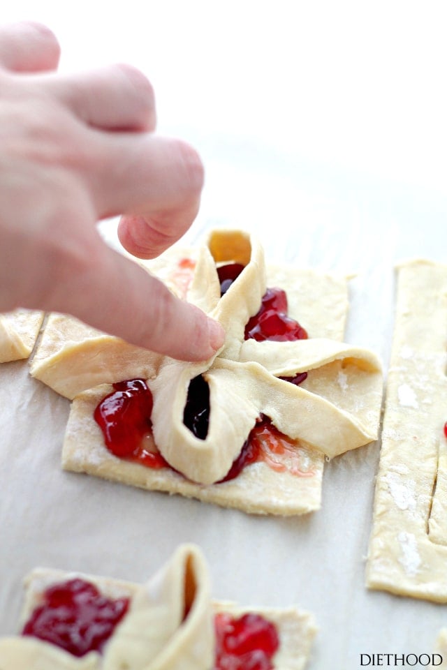 A hand shaping Puff pastry jam tarts into little bows.