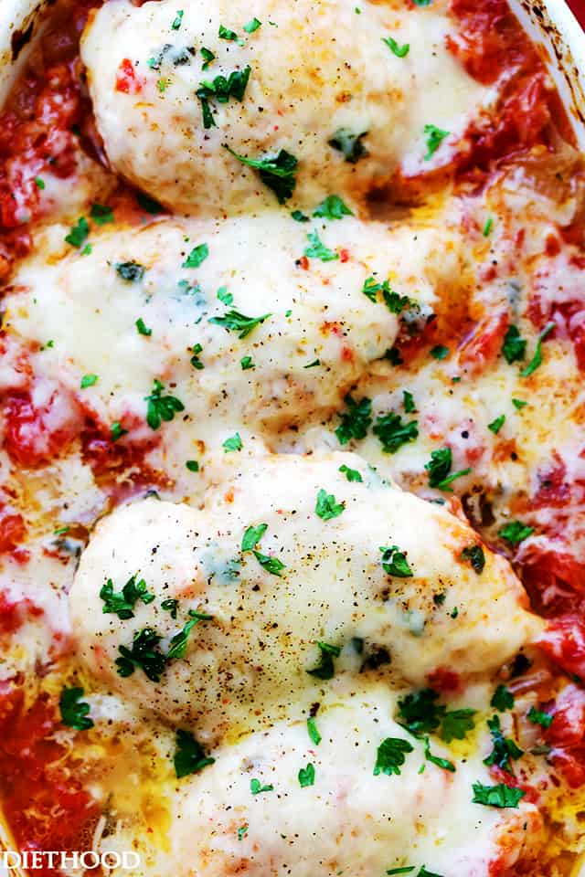 Close-up image of four chicken breasts nestled in tomato sauce and topped with melted gruyere cheese.