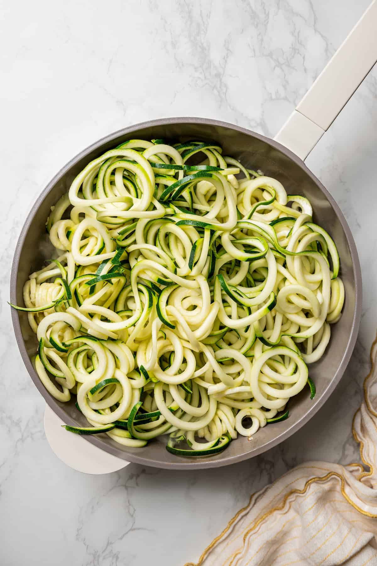 Spiralized zucchini noodles added to a skillet.