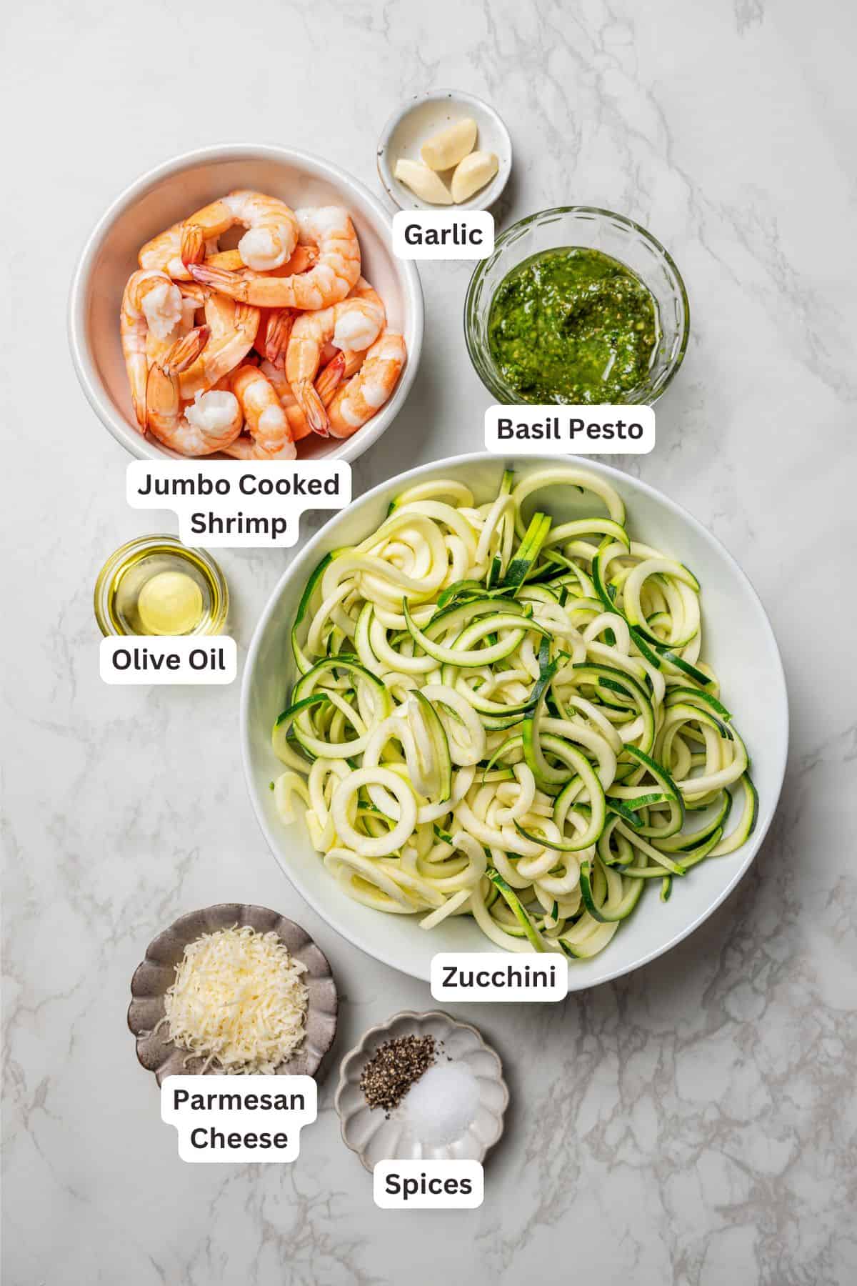 Ingredients for pesto zucchini noodles with shrimp, with text labels overlaying each ingredient.