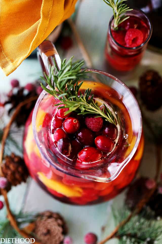 Overhead view of the mouth of a pitcher filled with cranberries, raspberries, and a rosemary sprig.