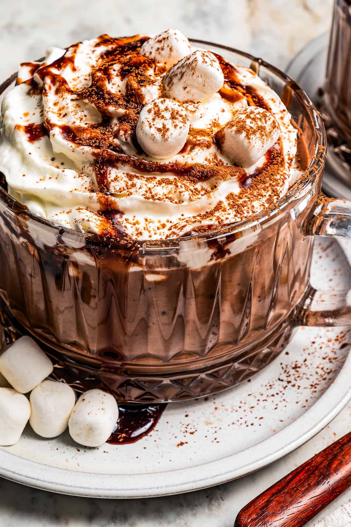 Close-up photo of hot chocolate in a glass mug topped with whipped cream and chocolate sauce.