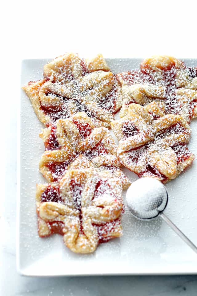 Puff pastries filled with raspberry jam arranged on a plate and dusted with powdered sugar.