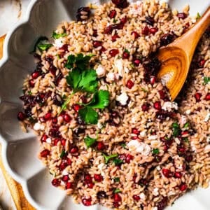 Orzo pasta salad in a large scalloped salad bowl with a wooden spoon.