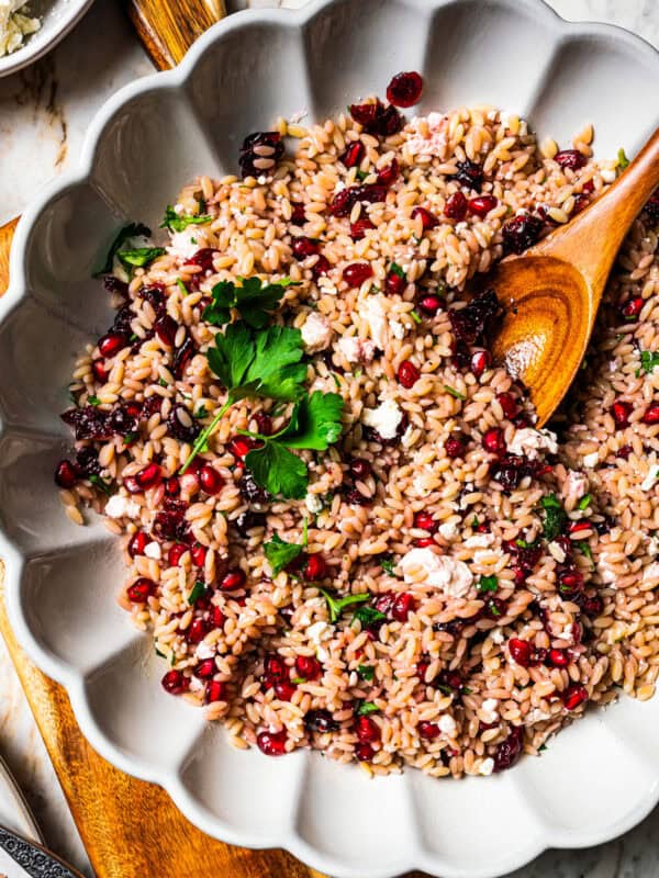 Orzo pasta salad in a large scalloped salad bowl with a wooden spoon.