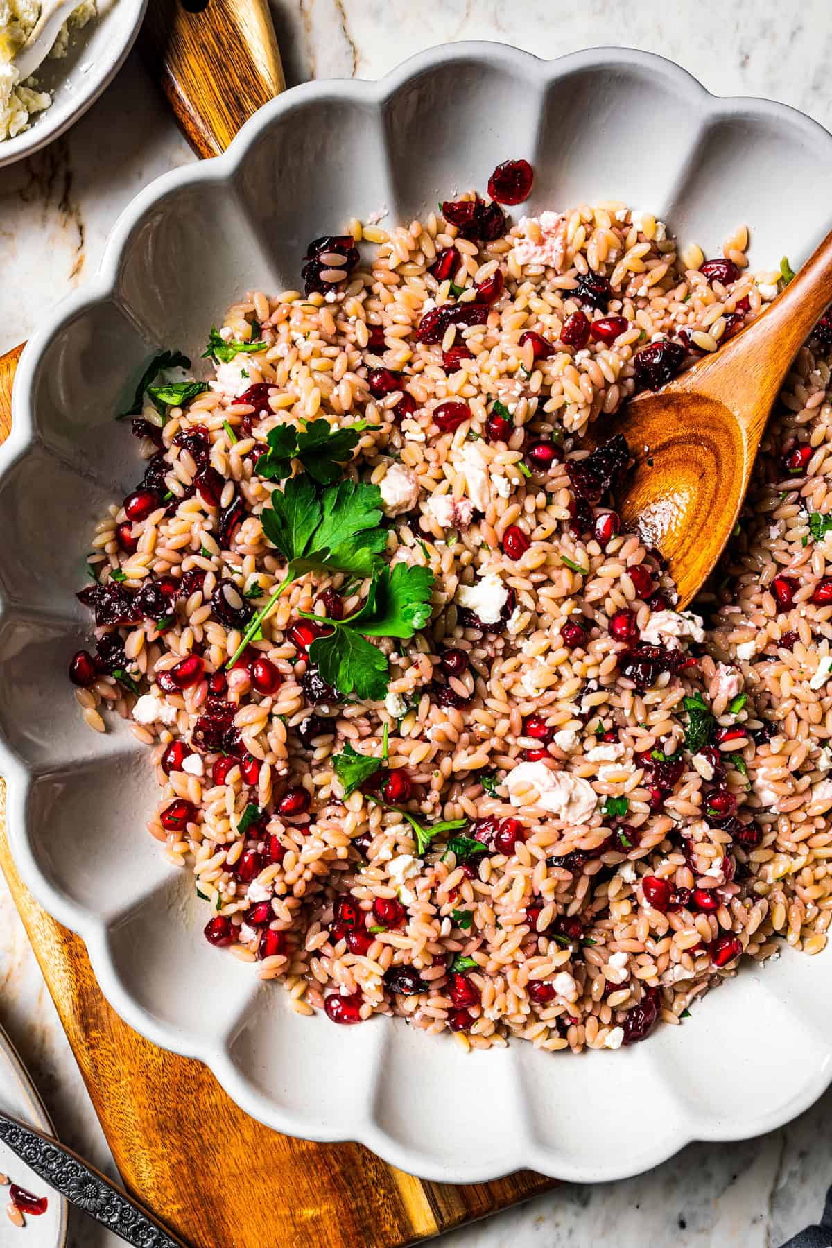 Orzo pasta salad in a large scalloped salad bowl with a wooden spoon.