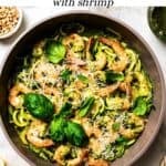 Text overlay over a photo of pesto zucchini noodles in a skillet with shrimp.