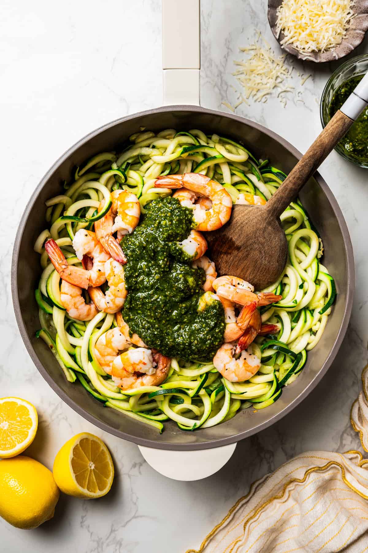 Stirring pesto into a skillet of zucchini noodles and shrimp.