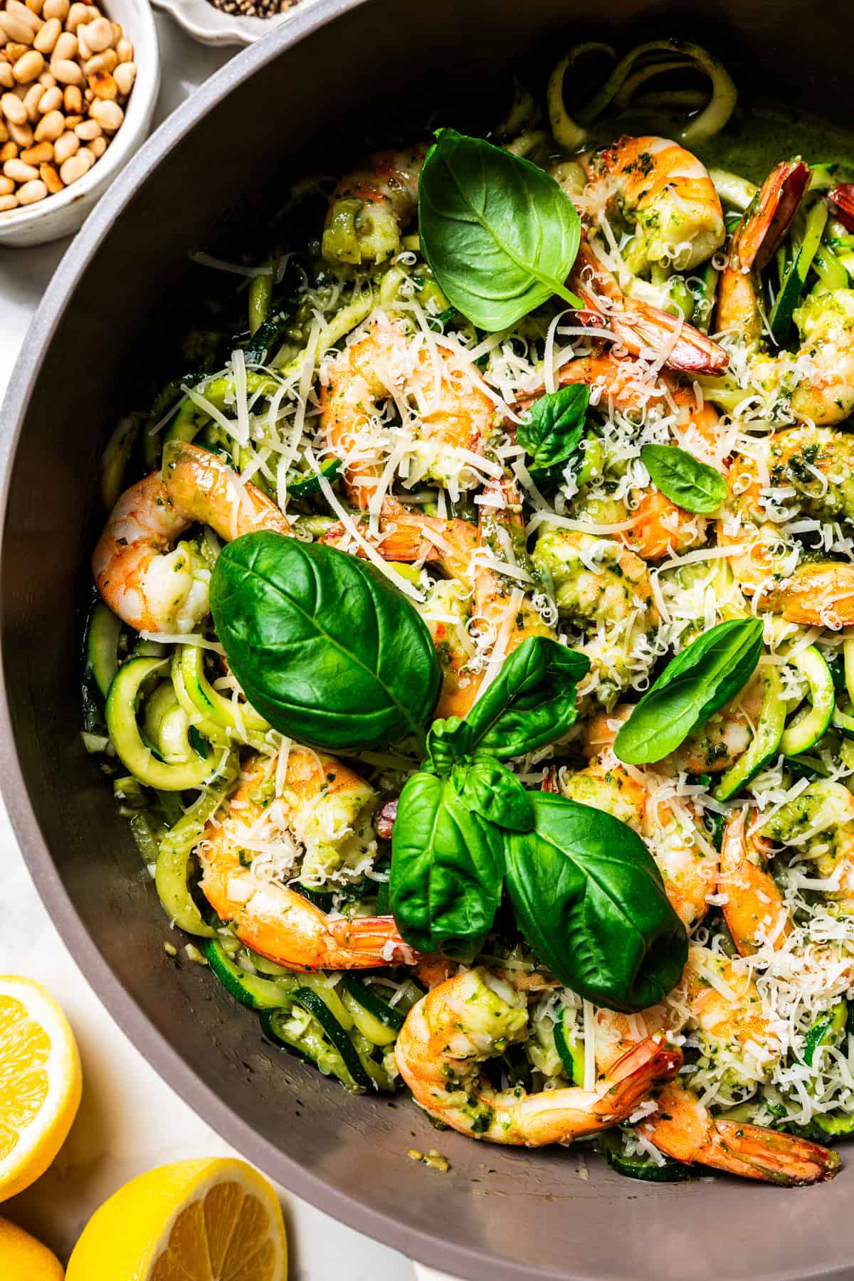 Zoodles in a skillet with shrimp and a garnish of parmesan cheese and fresh basil leaves.