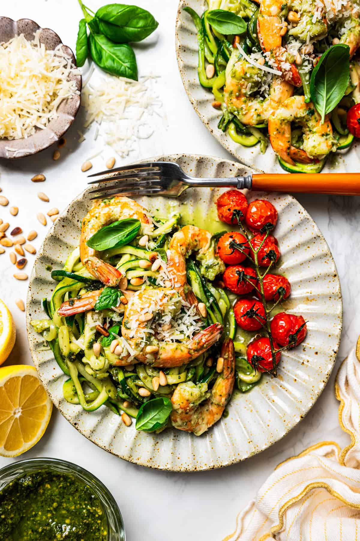 Pesto zucchini noodles served on two dinner plates, topped with shrimp and a side of cherry tomatoes.