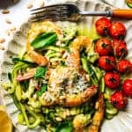 Pesto zucchini noodles served on a dinner plate with shrimp and cherry tomatoes.