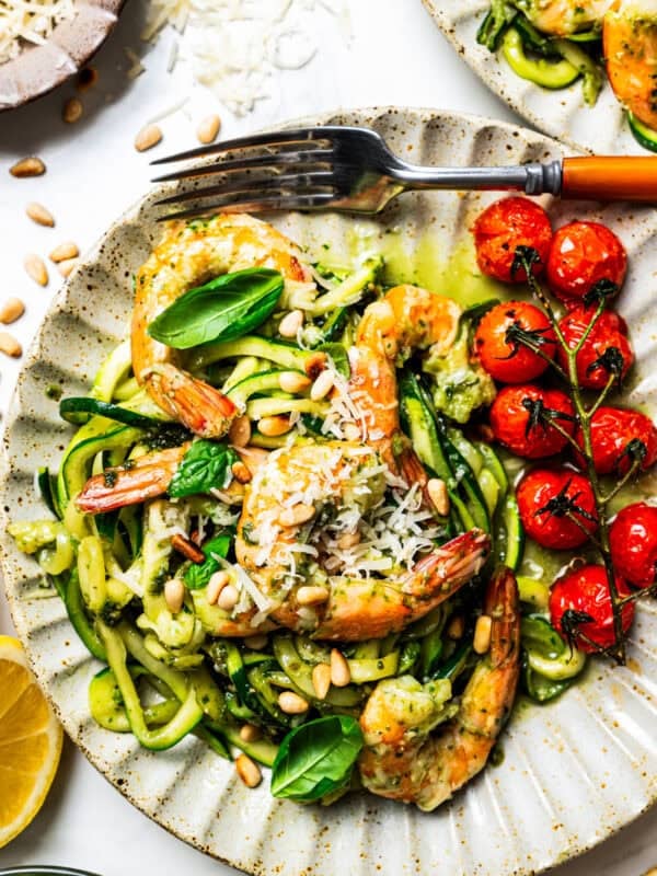 Pesto zucchini noodles served on a dinner plate with shrimp and cherry tomatoes.