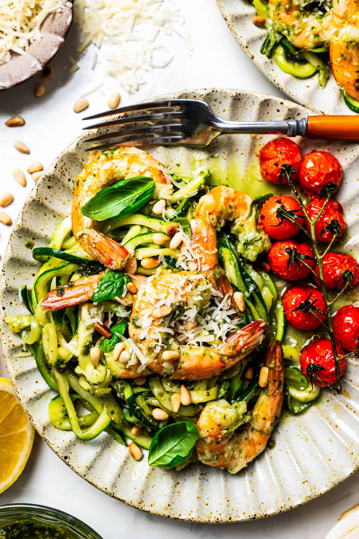 Pesto zucchini noodles served on a dinner plate with shrimp and cherry tomatoes.